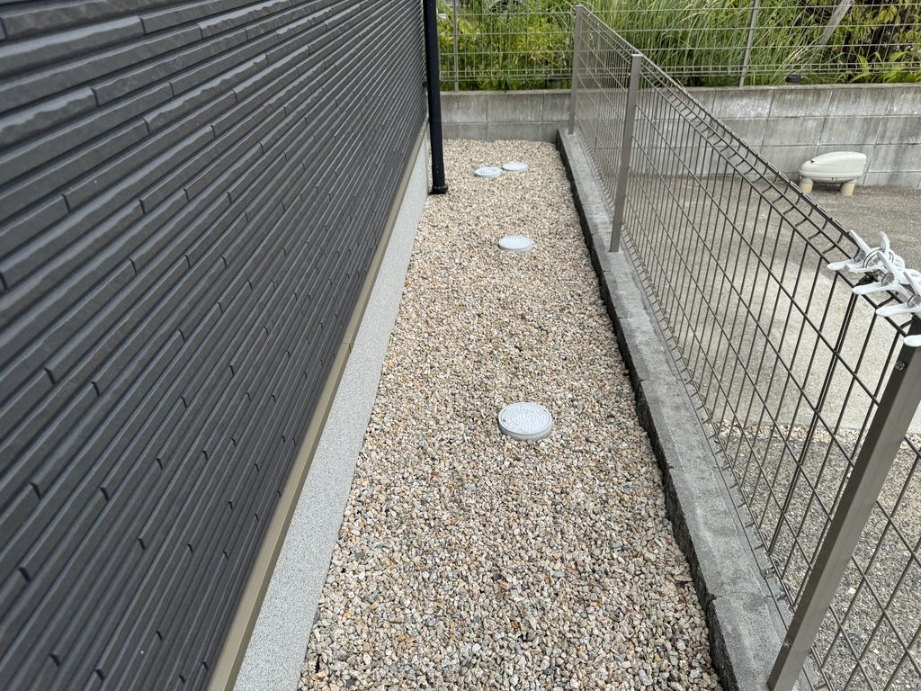 家の外周に防草シートと砂利を施工した様子。建物の外壁とメッシュフェンスの間に砂利が敷いてある